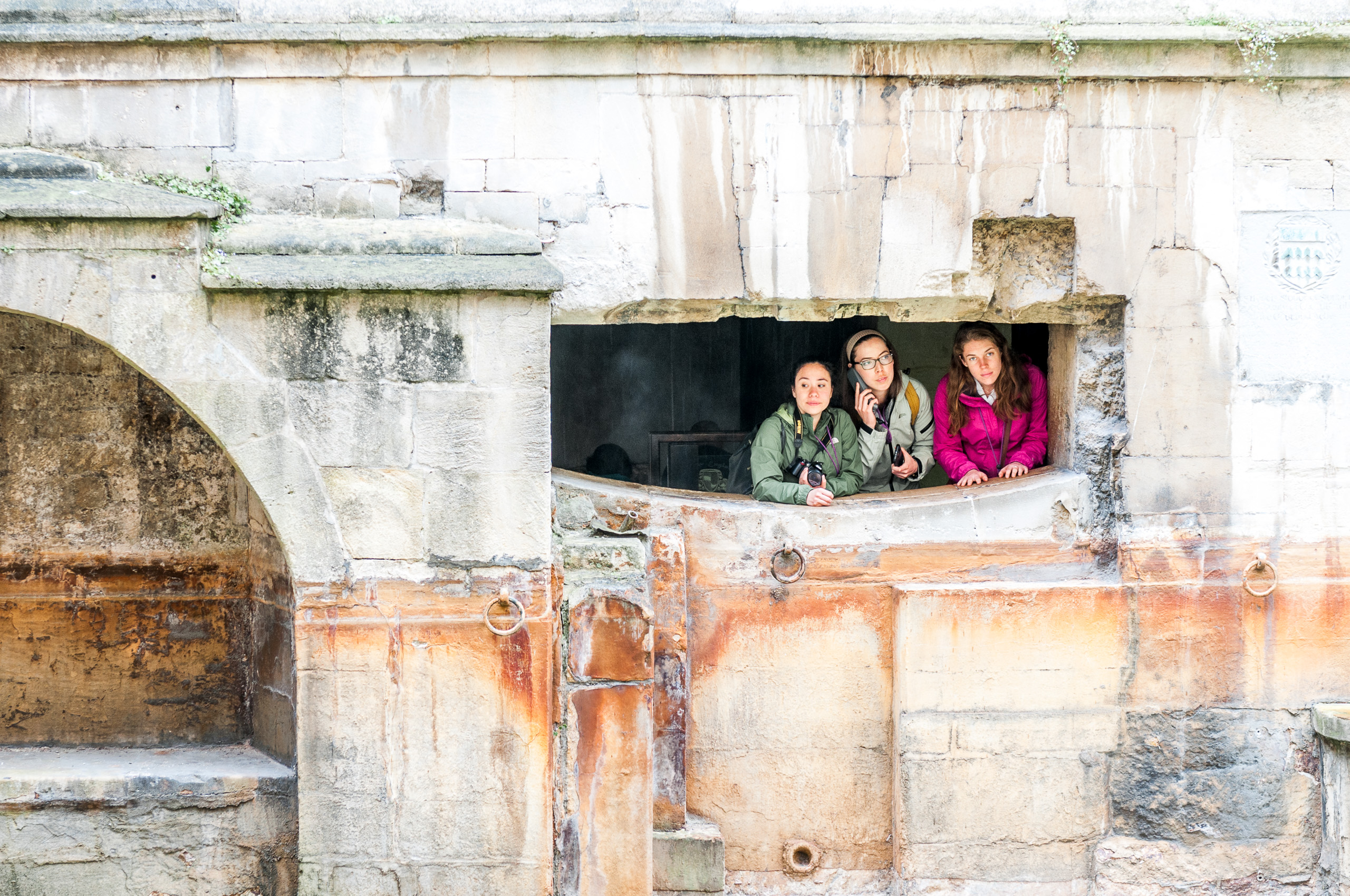 Three girls in colourful raincoats visiting the Roman Baths at Bath