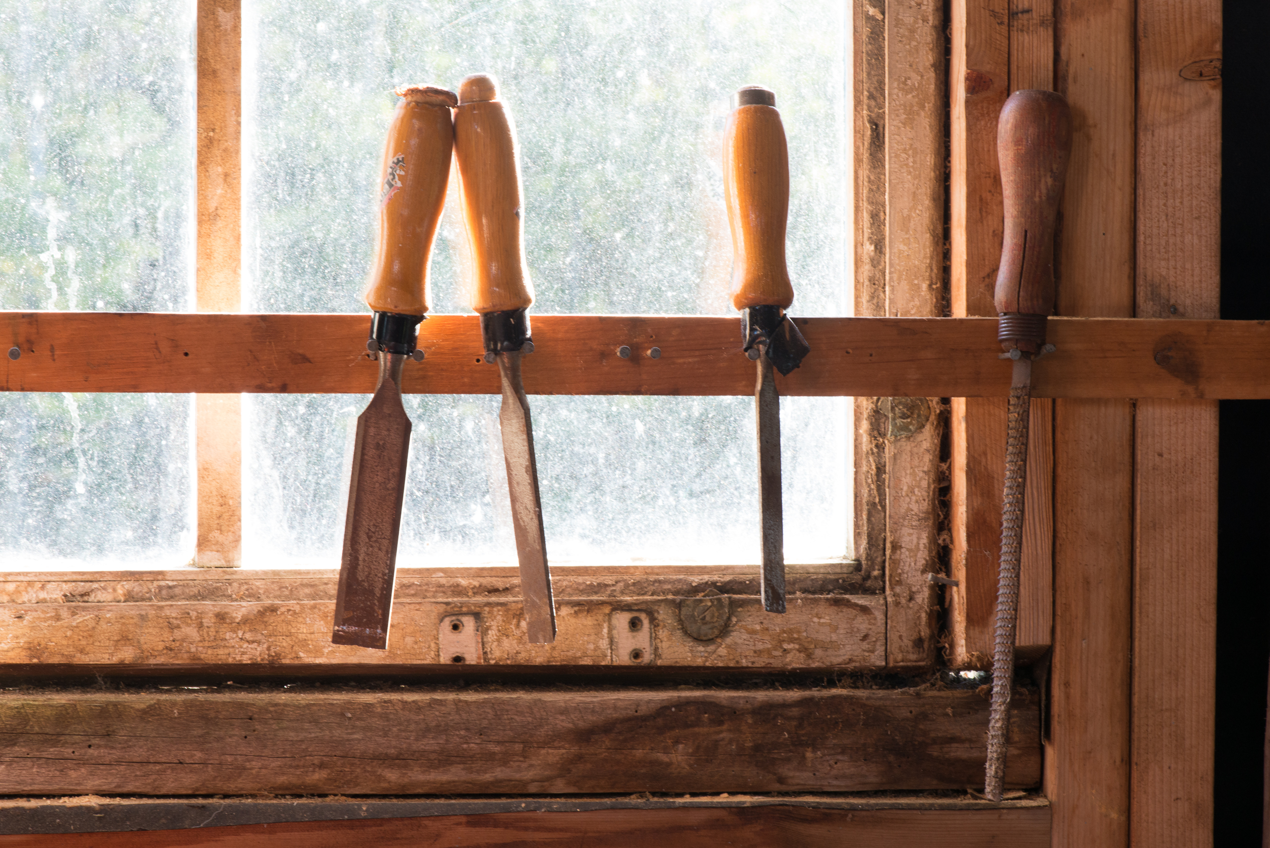 Three chisels and a rasp on a makeshift rack against a brightly lit window