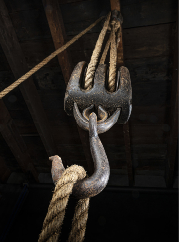 Old wooden hoist with forged hook and sisal rope.